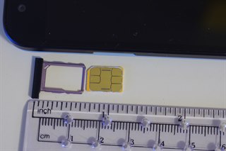 A nano SIM card and its tray beside a ruler for scale