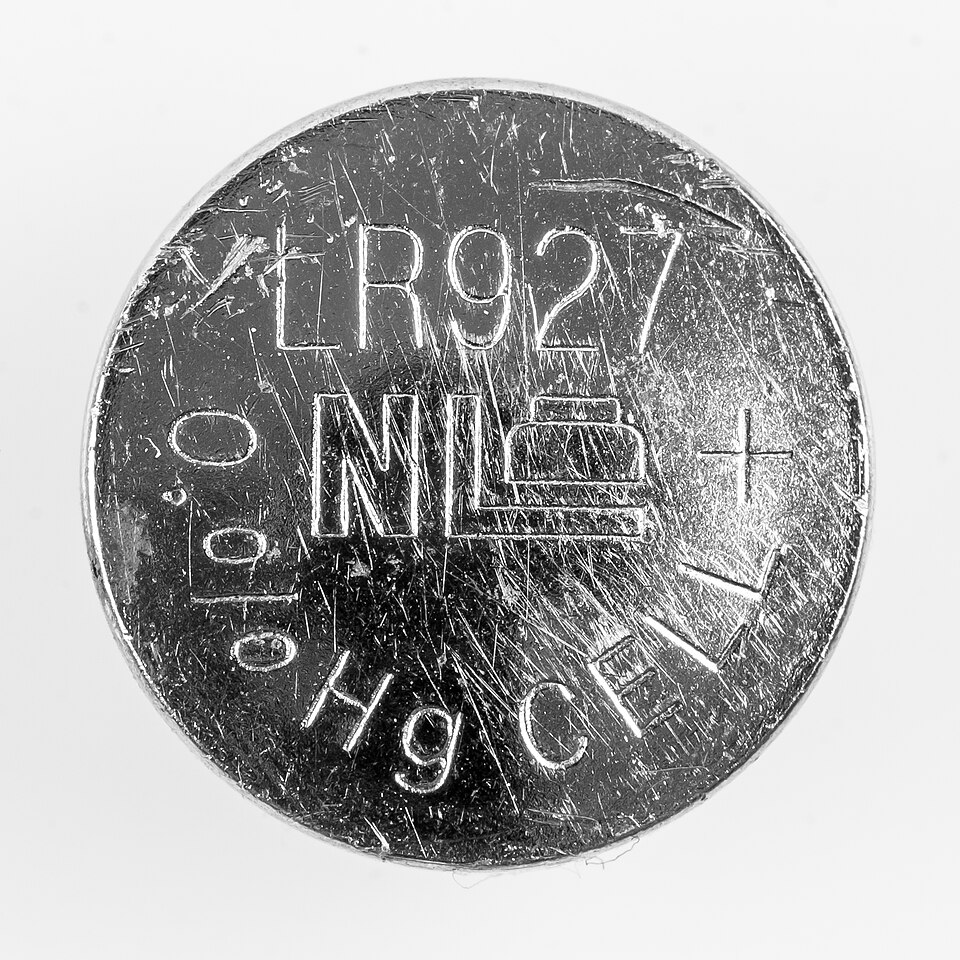 Close-up of an LR927 alkaline button cell lid engraved with LR927, a 0% Hg mark, and a plus sign