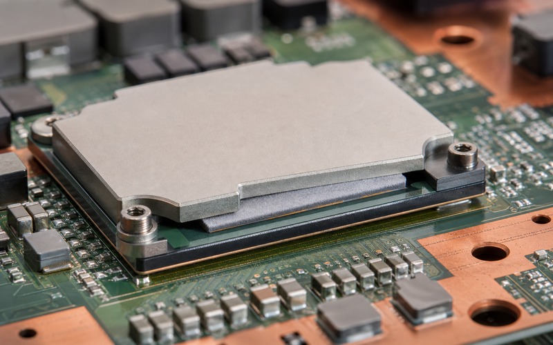 Thermal interface pad compressed between an AI processor package and an aluminum heat spreader, with copper spreading area, screw posts and surrounding power components on a clean PCB