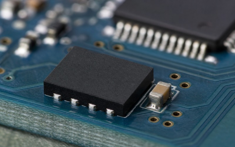 Low-angle macro of one WSON-8 serial flash package showing four leadless solder fillets, a nearby decoupling capacitor and ground vias