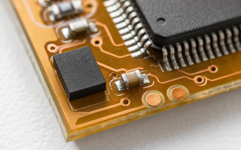 Extreme macro of one 2x3mm leadless USON flash on amber FR4 with a nearby ceramic capacitor, two test pads and short traces to a TQFP controller