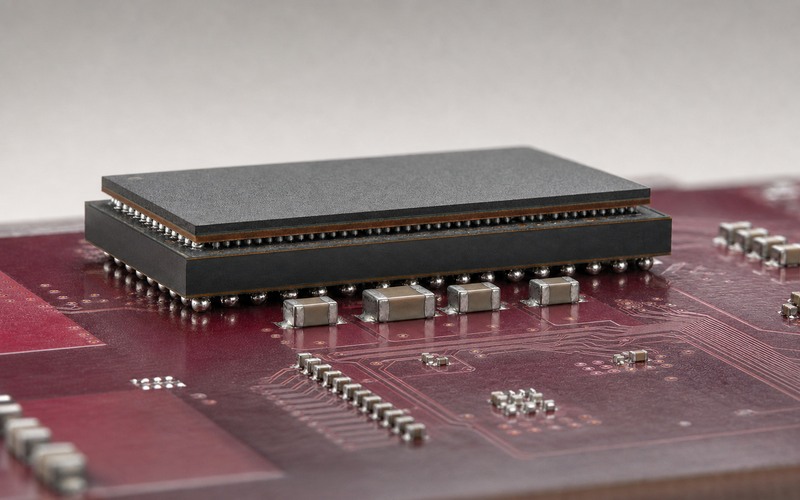 Low side view of one LPDDR5 package stacked over an application processor on a burgundy PCB, showing the two solder-ball interfaces and nearby decoupling capacitors