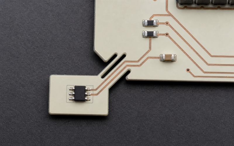 Top-down ivory PCB tab with a six-pin SOT563 temperature sensor, isolation slots and four copper traces