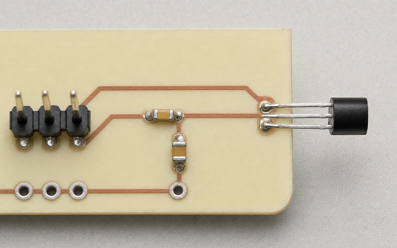Top-down cream PCB with one TO-92 temperature sensor at the outer edge and a short copper route through a small resistor-capacitor filter